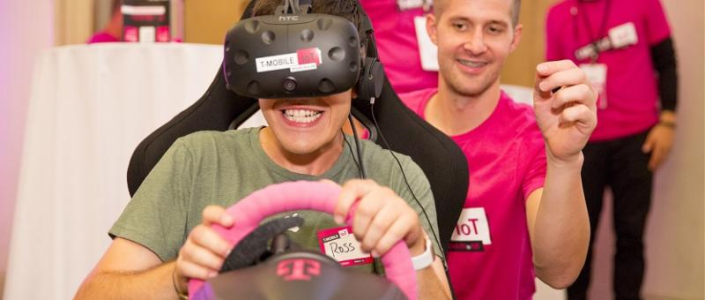 Event attendee driving a virtual reality car with T-Mobile event staff assisting in the background
